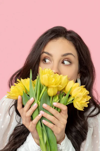 Jeune jolie femme aux cheveux bruns tenant des fleurs jaunes et l'air surpris — Photo