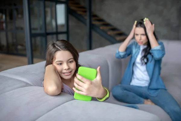 Chica sonriente sosteniendo un teléfono inteligente en sus manos y pasar tiempo en línea — Foto de Stock