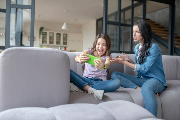 Девушка в джинсах показывает что-то на смартфуне своей маме
