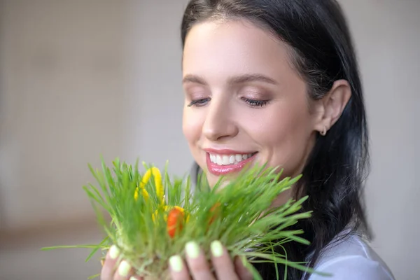 Brunette rayonnant femme souriant et regardant l'herbe dans ses mains — Photo