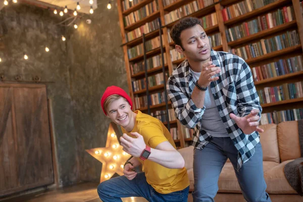 Ung man i gul tröja har kul med sin vän och ler — Stockfoto