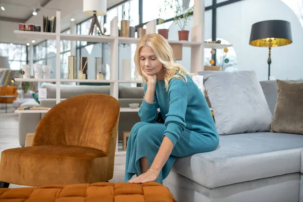 Mulher loira em um vestido azul tocando o sofá — Fotografia de Stock