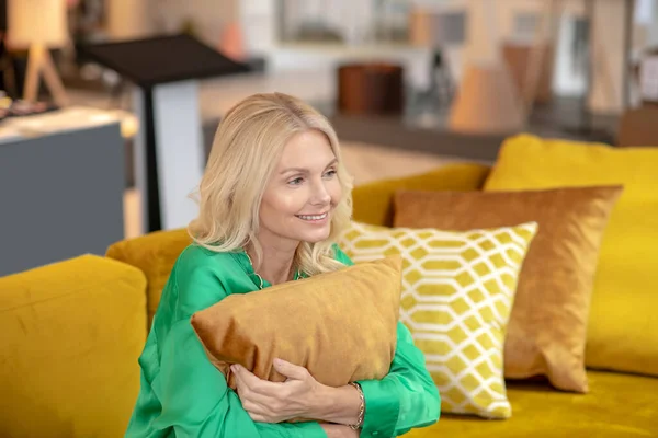 Donna bionda in una camicetta verde che abbraccia il cuscino e sorride — Foto Stock