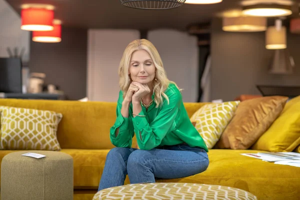 Блондинка в зелёной блузке сидит на жёлтом диване — стоковое фото