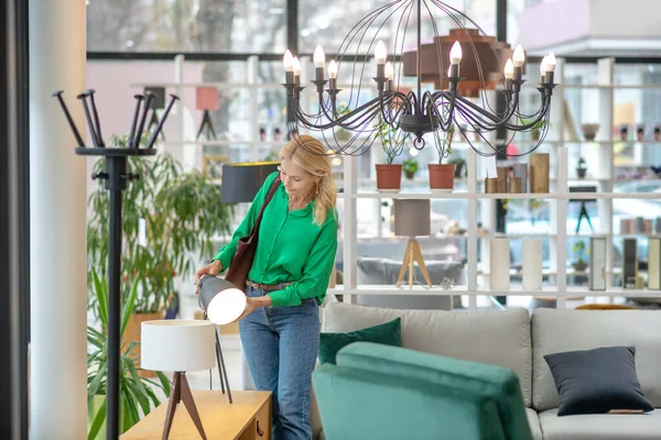 Blonde woman in a green blouse touching the lamp — Stock Photo, Image