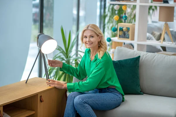Блондинка в зеленой блузке сидит рядом с лампой — стоковое фото