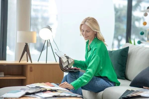 Блондинка в зеленой блузке сидит на диване — стоковое фото