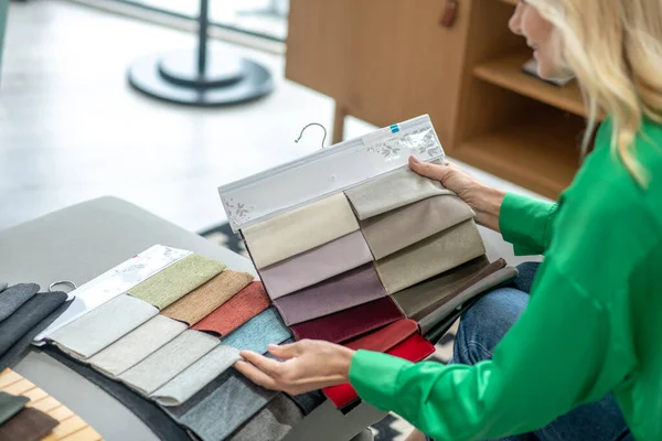 Mulher loira em uma blusa verde escolhendo tecido para móveis — Fotografia de Stock