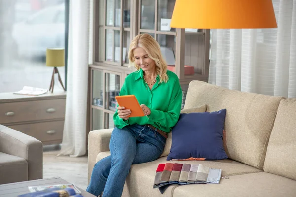 Blond-haired woman with a tablet sitting on the couch.