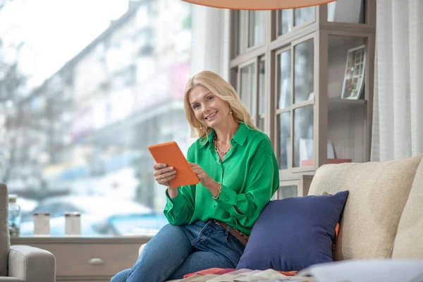 Joyful woman with a tablet sitting on the couch.