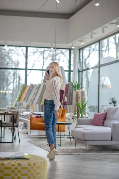 Mulher de jeans e mocassins brancos em pé em um salão de móveis . — Fotografia de Stock