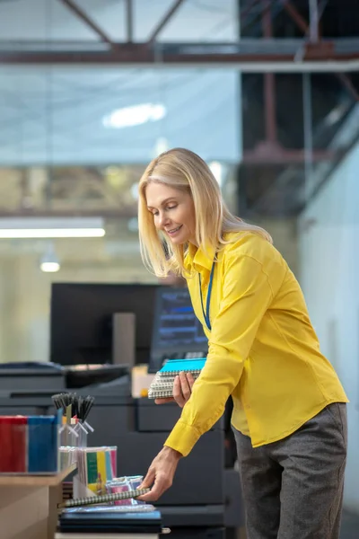 Blonde woman bending, laying out notebooks, smiling