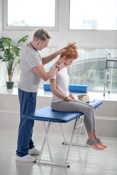 Fisioterapeuta masculino examinando el cuello de una paciente sentada en un sofá — Foto de Stock