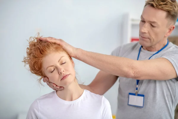 Manlig sjukgymnast som behandlar huvudet på en kvinnlig patient — Stockfoto