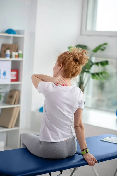 Paciente femenina pelirroja sentada en el sofá y masajeando su doloroso cuello — Foto de Stock