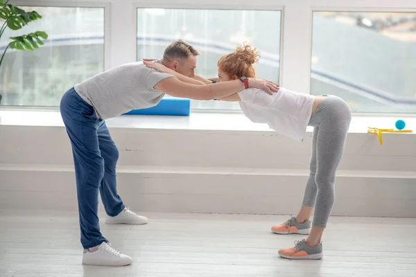 Patient féminin et physiothérapeute masculin debout demi-flexion vers l'avant pose — Photo