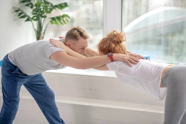 Female patient and male physiotherapist standing half forward bend pose — Stock Photo, Image