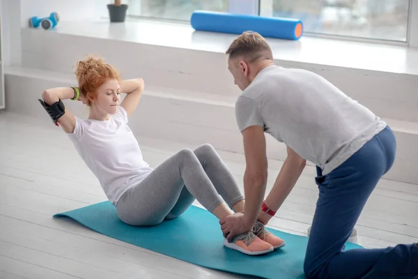 Vrouwelijke patiënt doet sit-ups op mat, mannelijke fysiotherapeut helpen haar door het houden van haar enkels — Stockfoto
