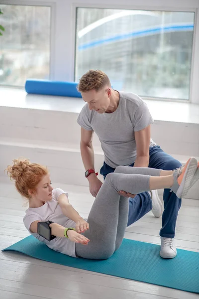 Kadın hasta mindere kıvrılıp yatıyor, erkek fizyoterapist dizlerini tutarak ona yardım ediyor.