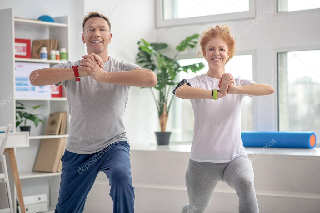 Female patient and male physiotherapist lunging synchronically, smiling