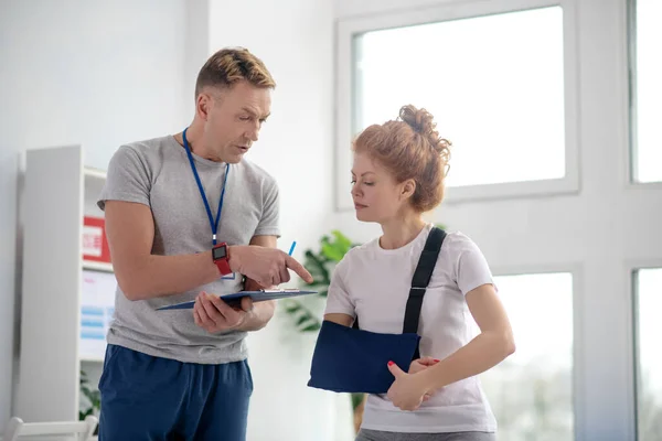 Male physiotherapist giving instructions to female patient with arm sling