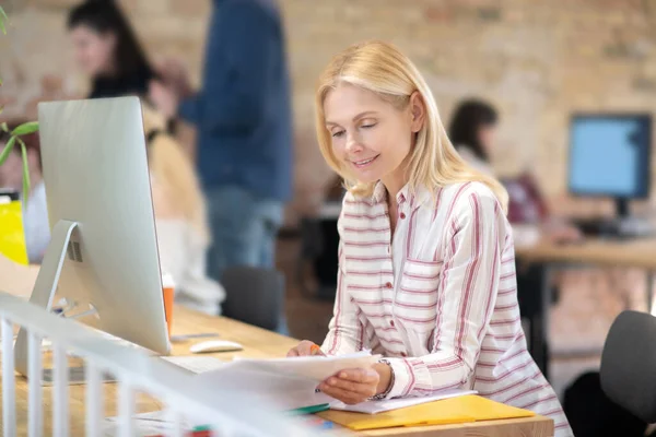 Blond kvinna sitter vid skrivbordet och kollar anteckningar — Stockfoto