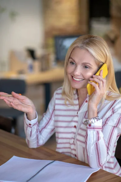 Mujer rubia sentada en el escritorio, teniendo una alegre conversación telefónica — Foto de Stock