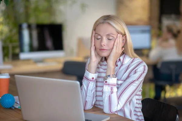 Mujer rubia sentada en el escritorio, sosteniendo templos — Foto de Stock