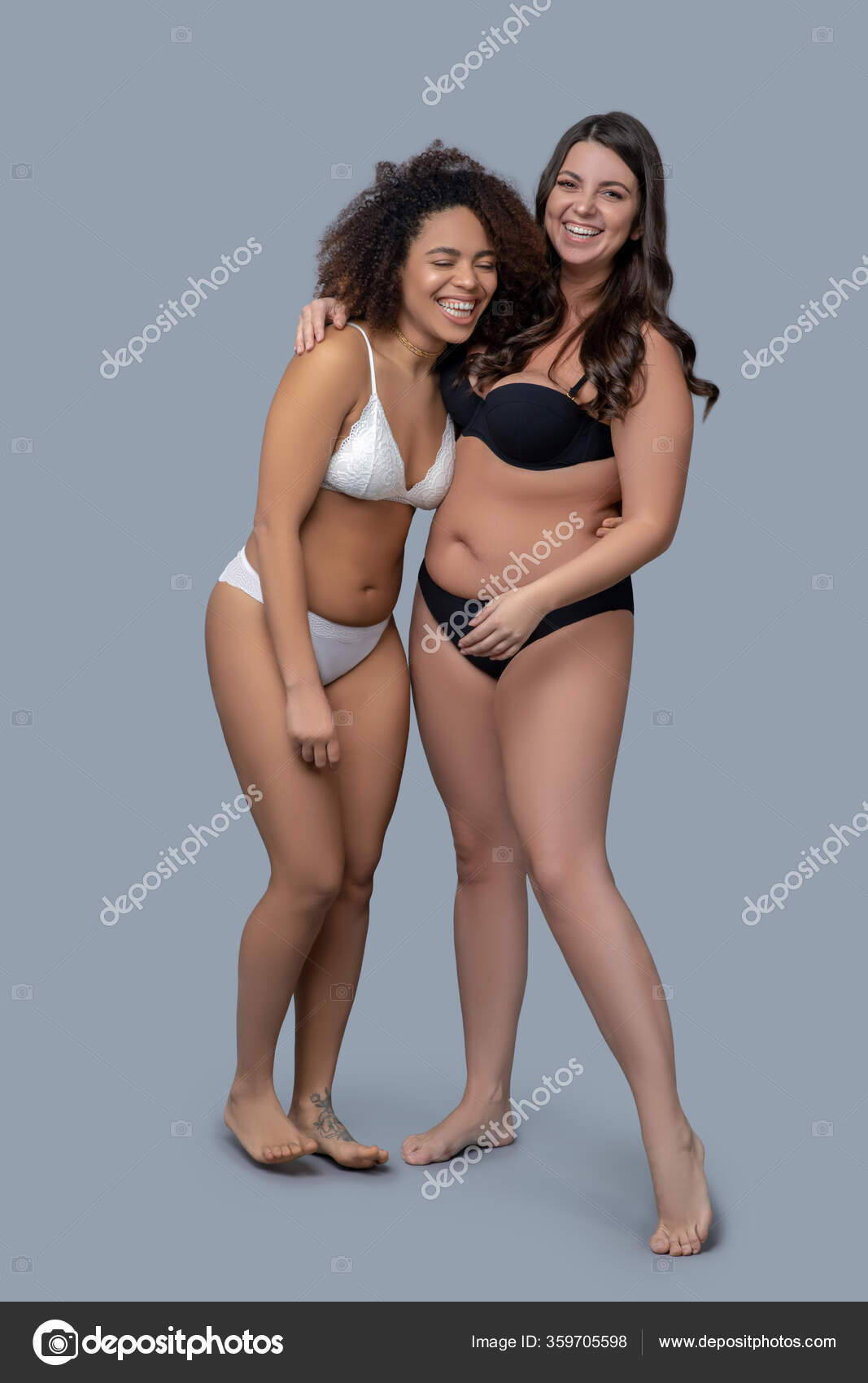 Two women in lingerie standing together on brown background. Young