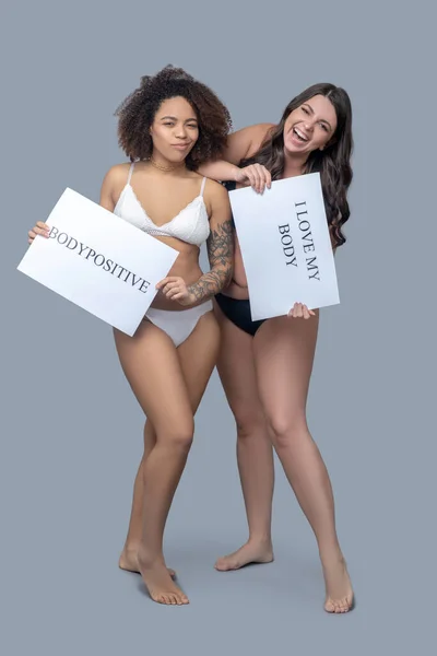 Duas mulheres mostrando cartazes com um slogan positivo . — Fotografia de Stock