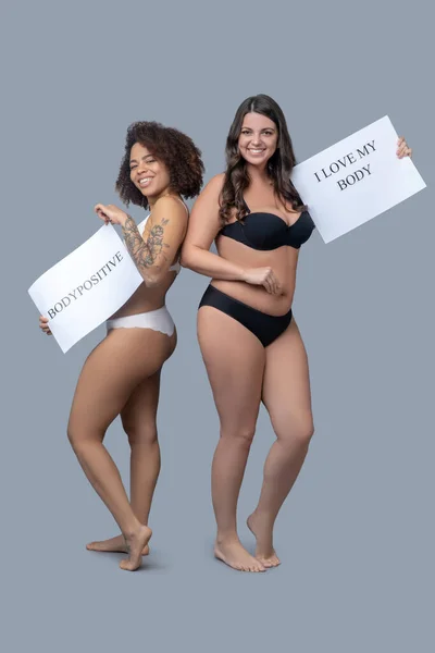 Girlfriends in linen barefoot with posters calling for self-perception. — Stock Photo, Image