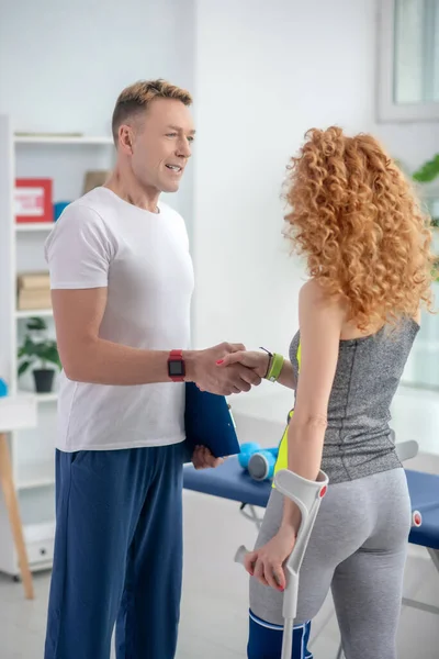 Fisioterapeuta masculino sorrindo e geeting paciente do sexo feminino com muleta — Fotografia de Stock