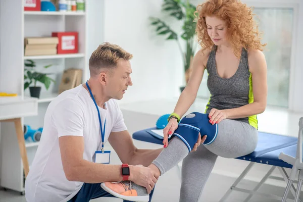 Male physiotherapist examining leg of female patient sitting on couch — Stock Photo, Image
