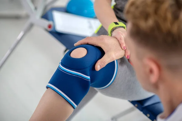 Αρσενικός φυσιοθεραπευτής χέρια εξέταση επίδεσμο γόνατος του ασθενούς γυναίκα — Φωτογραφία Αρχείου