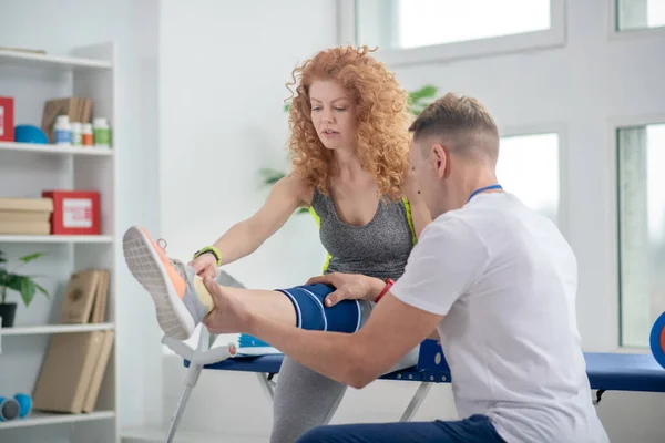 Fisioterapeuta masculino examinando vendaje de rodilla y pierna de paciente femenino —  Fotos de Stock
