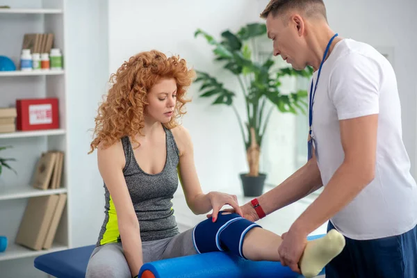 Male physiotherapist examining knee injury of female patient — Stock Photo, Image