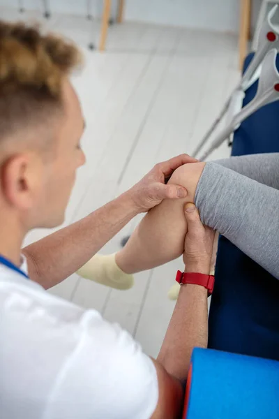 Mužské fyzioterapeutické ruce léčí poranění kolene pacientky — Stock fotografie
