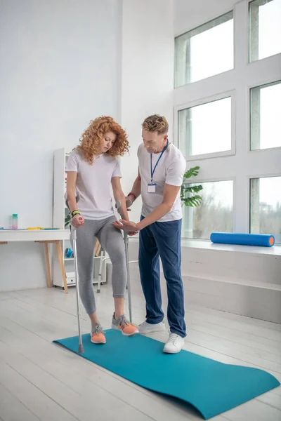 Fisioterapeuta masculino ajudando paciente feminino a andar com muletas — Fotografia de Stock