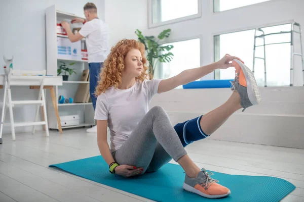 Vrouwelijke patiënt zittend op mat en strekkend haar been — Stockfoto