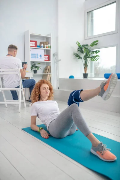Vrouwelijke patiënt liggend op mat en buigen haar been — Stockfoto