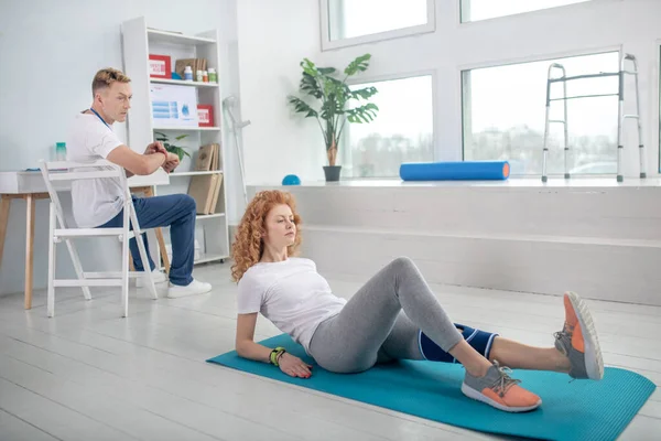 Vrouwelijke patiënt liggend op mat en stretching haar been — Stockfoto