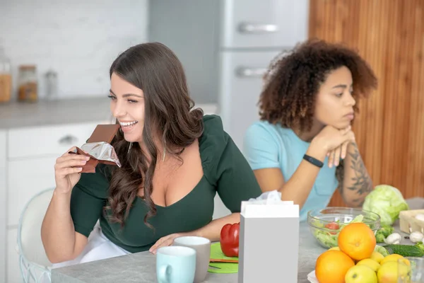 Smiling woman with chocolate, the second sad with curly hair. — Stock Photo, Image