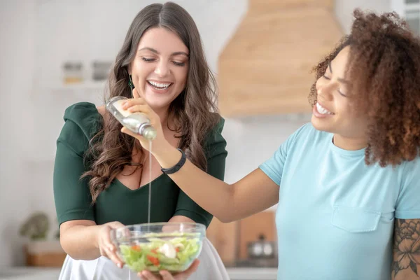 Две женщины добавляют салатное масло в овощной салат . — стоковое фото
