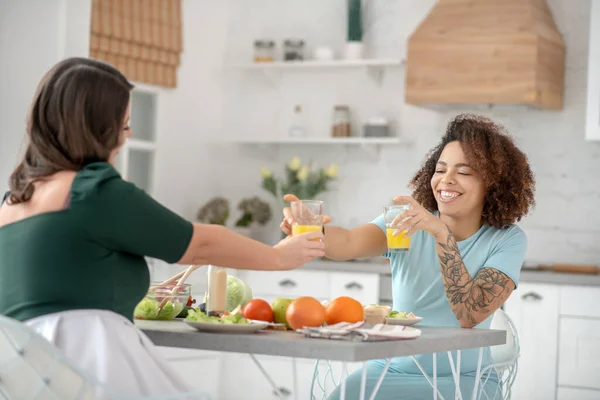 Woman giving a glass of juice to her girlfriend.