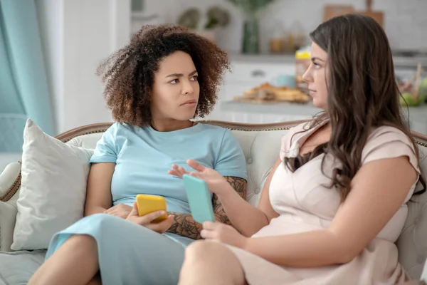 Dos mujeres jóvenes con smartphones en las manos sentadas en un sofá . — Foto de Stock