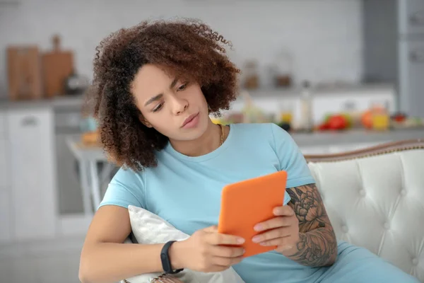 Mujer seria sentada en un sofá mirando una tableta . — Foto de Stock