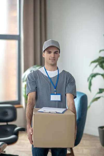 Entrega courrier en una gorra de pie con una gran caja en sus manos — Foto de Stock