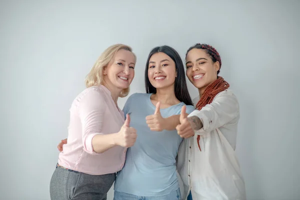 Drie vrouwen die glimlachend bij de muur staan — Stockfoto