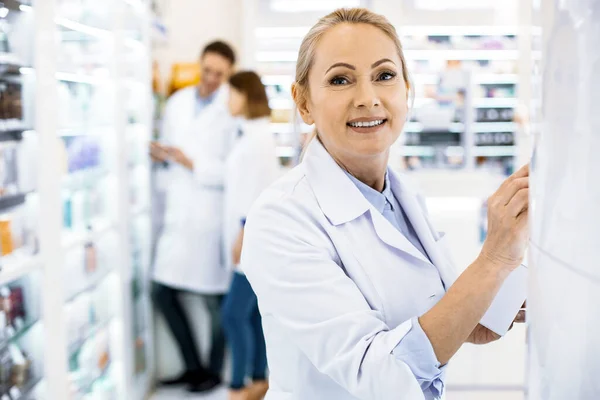 Vonzó női gyógyszerész felülvizsgálata polcon egy gyógyszertárban — Stock Fotó