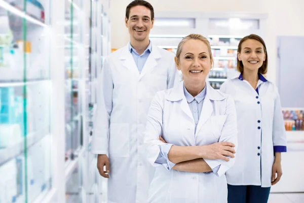 Счастливые три молодых фармацевта приветствуют клиентов улыбаясь — стоковое фото